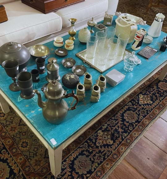 Mesa de centro turquesa com coleção de peças utilitárias e decorativas antigas, como bules, copos, taças e porcelanas, em ambiente de móveis usados na Coar.