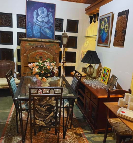 Sala de jantar com mesa de vidro, cadeiras estampadas, arranjo floral e quadros decorativos, compondo acervo de móveis e arte
