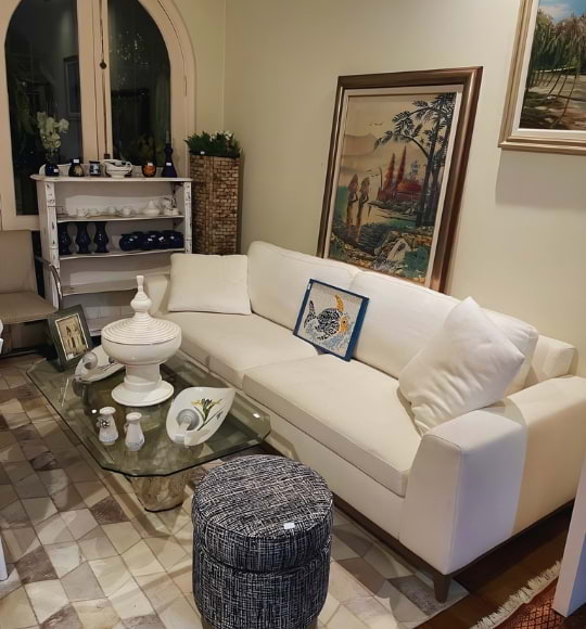 Sala decorada com sofá branco, mesa de centro em vidro, peças de porcelana e quadros, compondo ambiente elegante e aconchegante