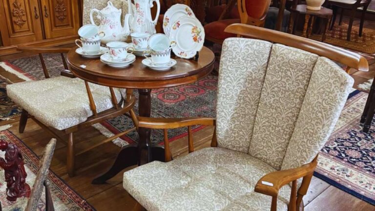 Sala com móveis antigos de madeira, cadeiras estofadas e mesa redonda decorada com louças, combinando estilo retrô com o contemporâneo