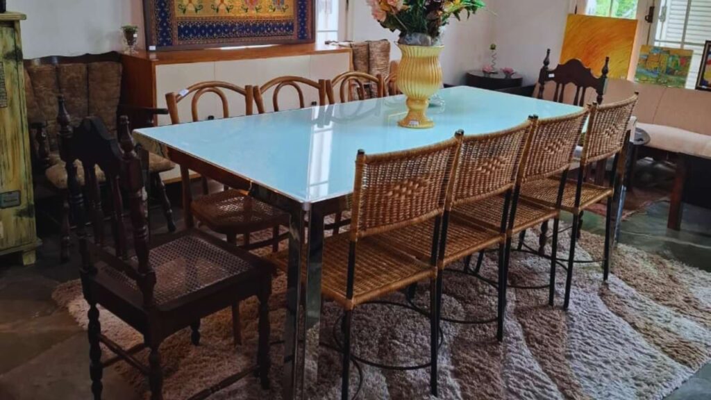 Sala de jantar com mesa de vidro moderna combinada com cadeiras antigas de madeira e palhinha, integrando móveis antigos e modernos na decoração